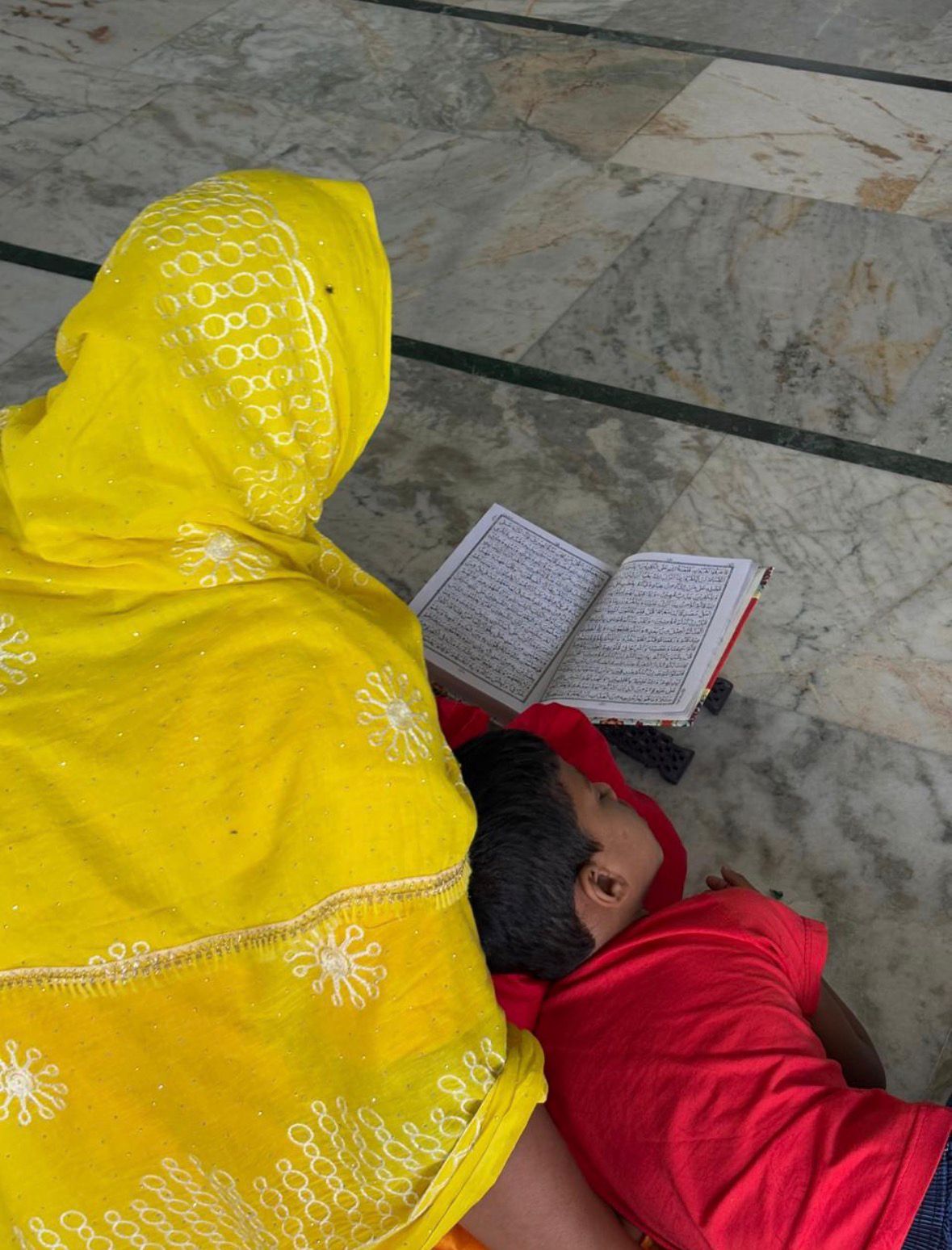 Mother reading Islamic testaments while her son enjoys the afternoon nap.